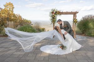 Groom dips bride in a romantic kiss outdoors near a wooden arch with floral decor and sweeping veil at Mountain Creek in Vernon, NJ.