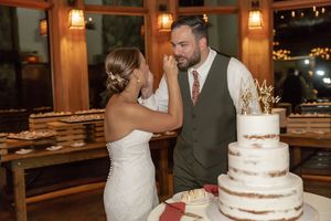 Bride feeding groom wedding cake at rustic reception beside elegant semi-naked tiered cake at Mountain Creek in Vernon, NJ.
