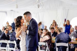 Bride and groom sharing intimate first dance under white tent surrounded by seated wedding guests at The Estate at Eagle Lake.