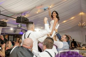 Bride lifted by groomsmen during lively wedding reception celebration under decorated tent venue at The Estate at Eagle Lake.