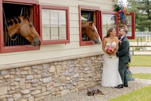 Bride and groom share a tender moment outside a stable with horses looking through the windows at Tourelay Farm in Colts Neck, NJ.