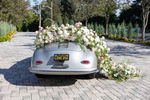 Silver vintage Porsche 356 wedding car decorated with cascading pink and white floral arrangement on trunk.