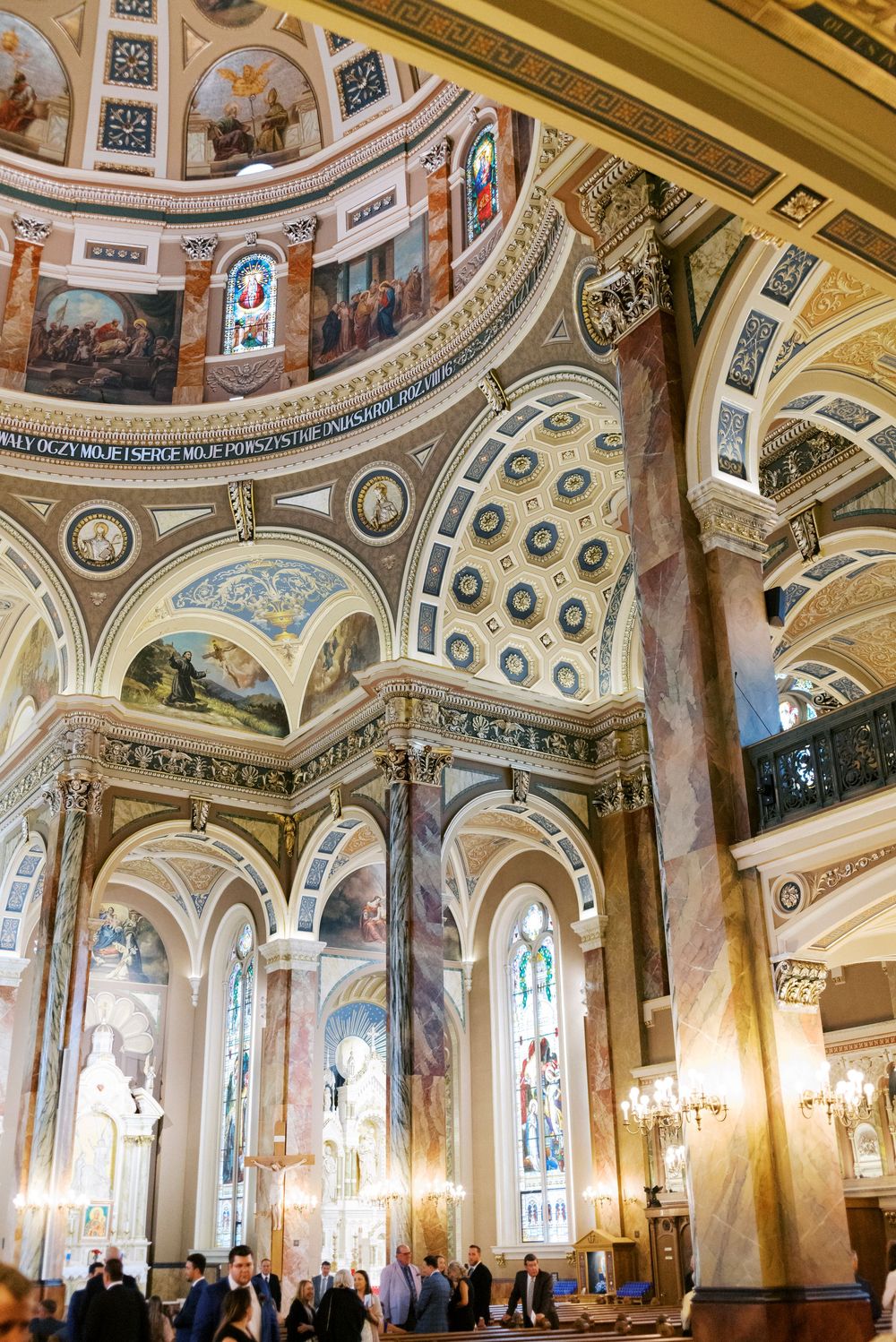 Ornate cathedral interior with frescoed arched ceilings, marble columns, stained glass windows, and intricate gold detailing.