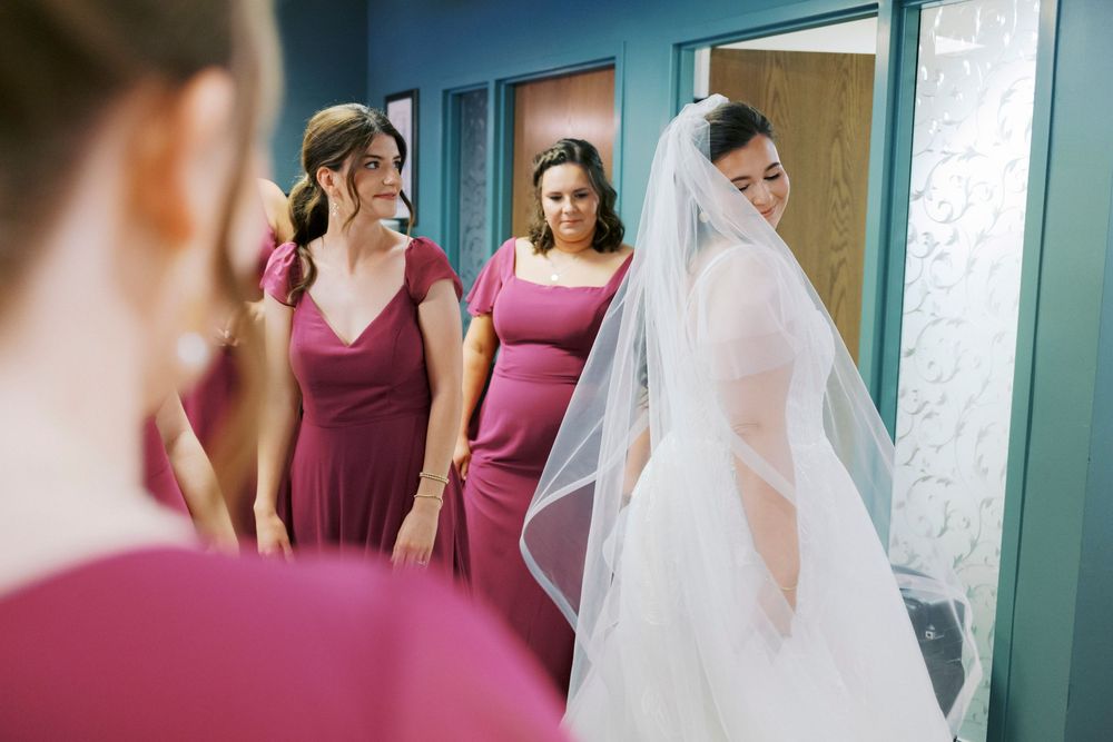 Midwest bride in white gown and veil with bridesmaids in burgundy dresses preparing for wedding ceremony.