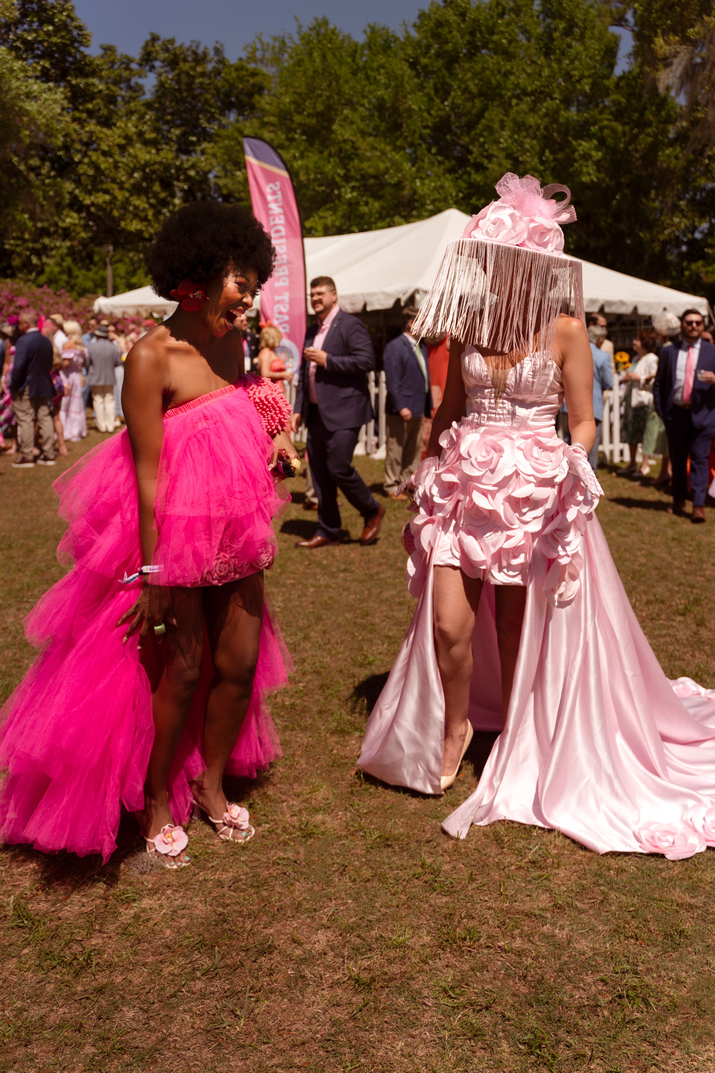 Two women in pink outfits at Airlie Gardens Azalea Festival, Lanatria in hot pink tulle dress, other in light pink gown with feathered hat.