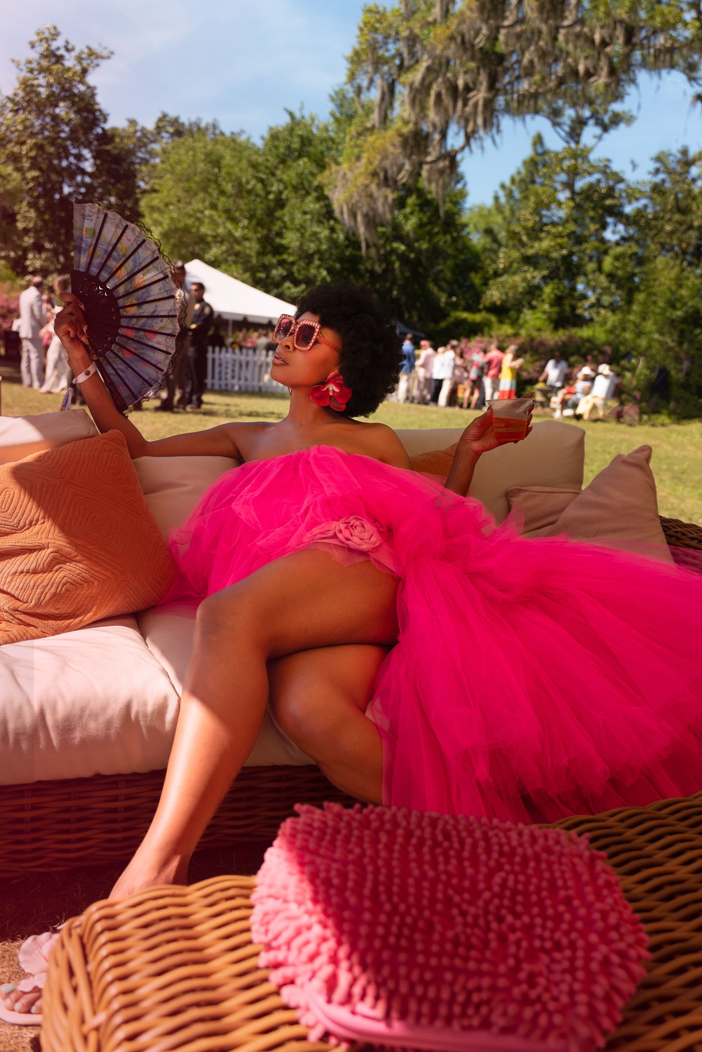 Lanatria aka Caribbean Cowgirl in pink tulle dress at Airlie Gardens Azalea Festival Garden Party holding a fan and wearing sunglasses .