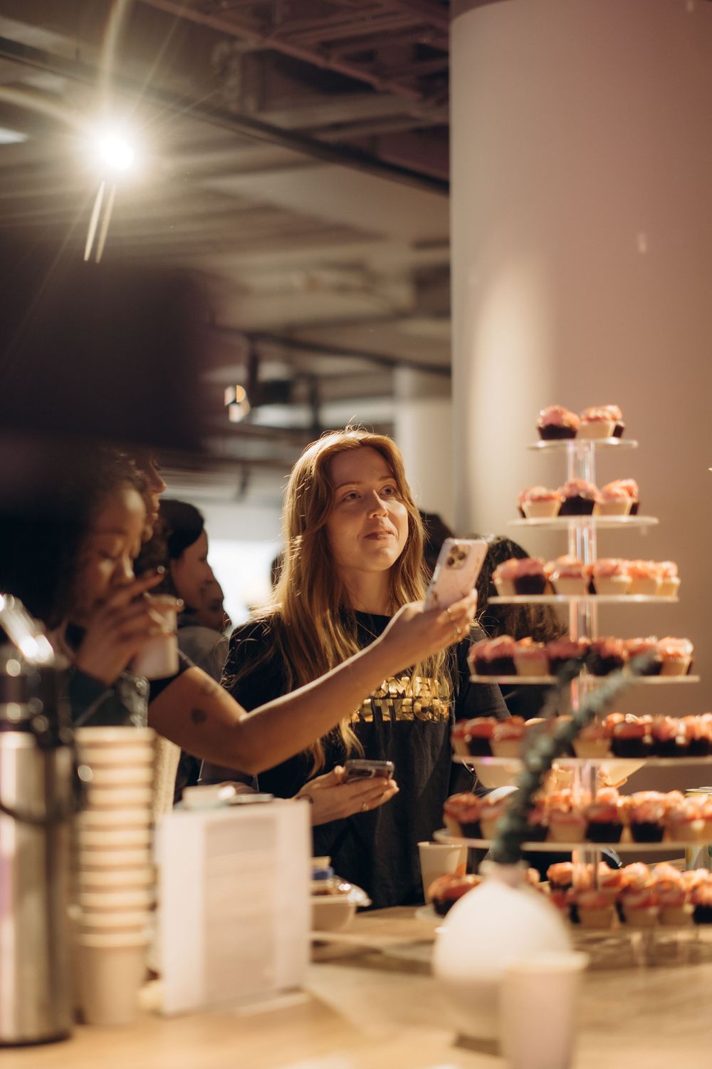 two women taking a photo of cupcakes during conference in Stockholm while being captured by business event photographer in Stockholm
