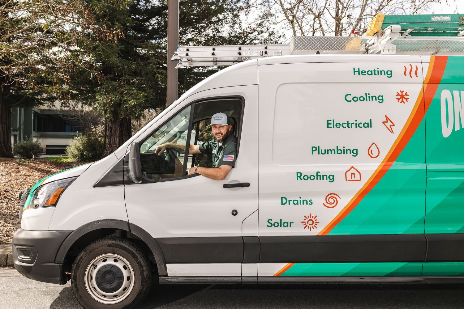 Smiling technician driving a branded service van offering heating, cooling, electrical, plumbing, roofing, drains, and solar services.