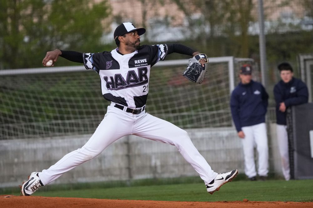 Baseball pitcher in white HAAR uniform mid-throw on the mound during a game.