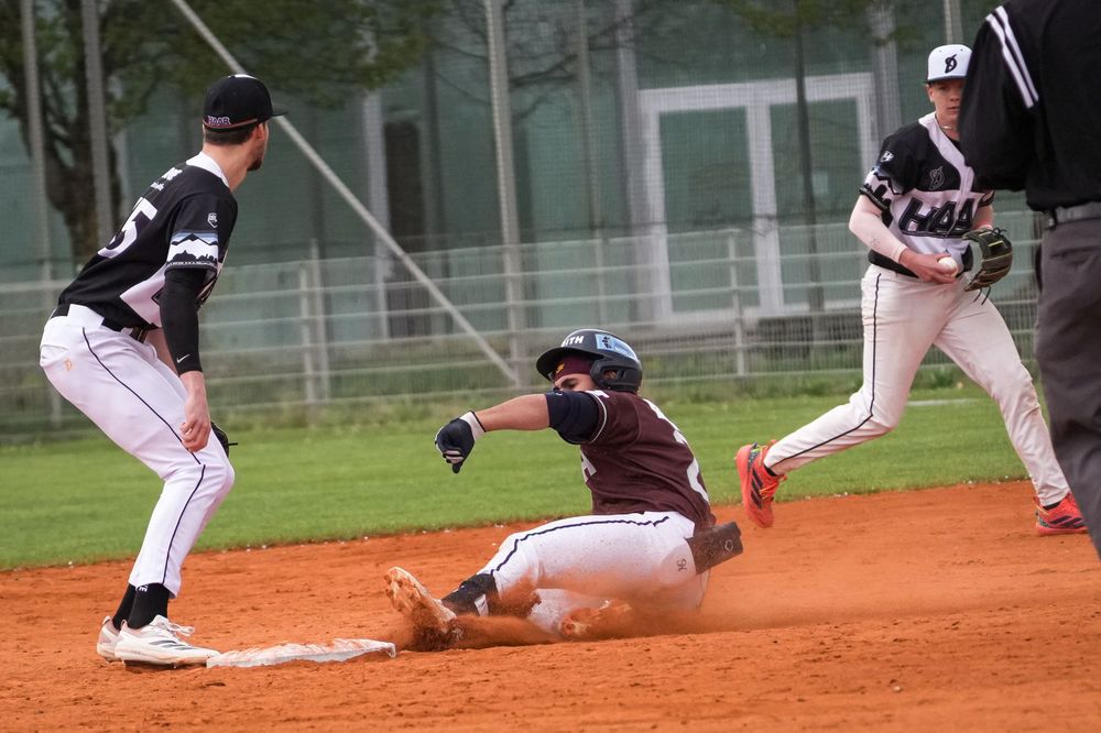 Baseball player sliding into base as fielder waits for the tag during a game on a dirt infield.