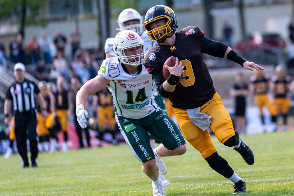 Two American football players in action, one in green jersey number 14 chasing a player in black and yellow uniform.