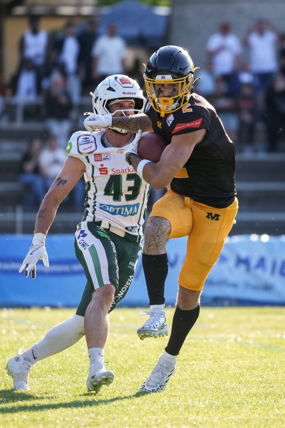 Two American football players in action, one in green jersey #43 and one in black and yellow uniform carrying the ball.