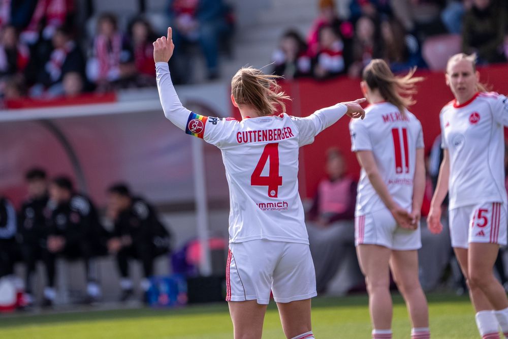 Female soccer player Guttenberger wearing number 4 raises her arm on the field during a women's football match.