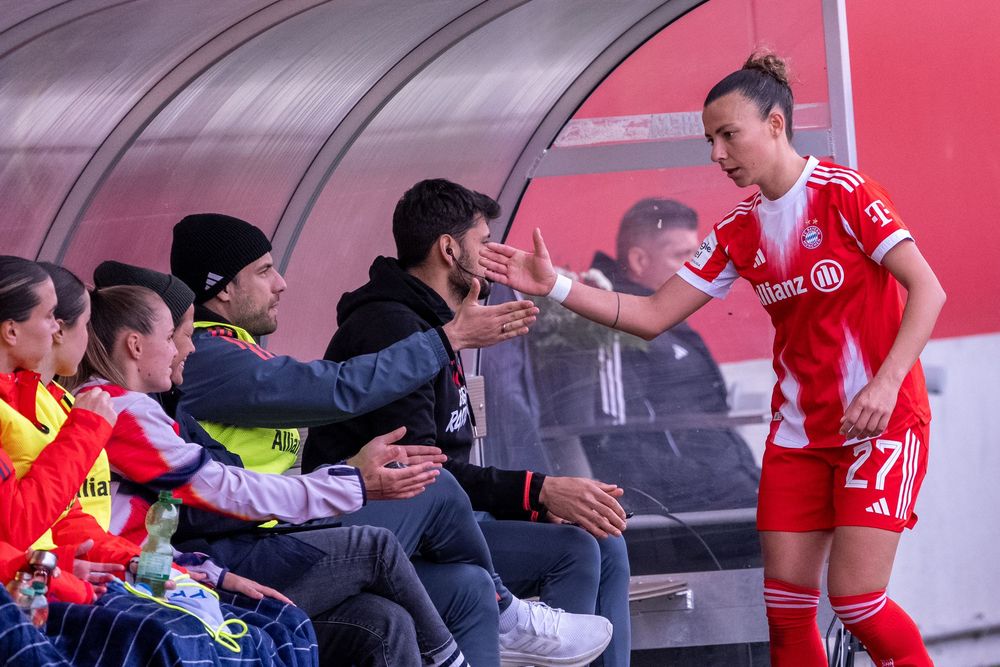 Female soccer player #27 in red uniform high-fiving fans on the sideline bench during a match.