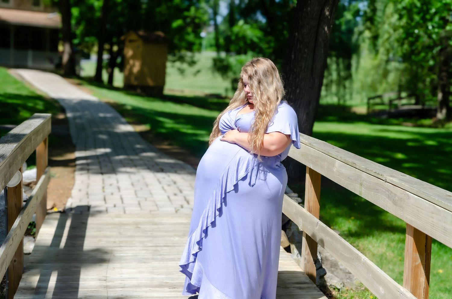 Pregnant woman in lavender maxi dress holding a baby outside a stone building with a red door.