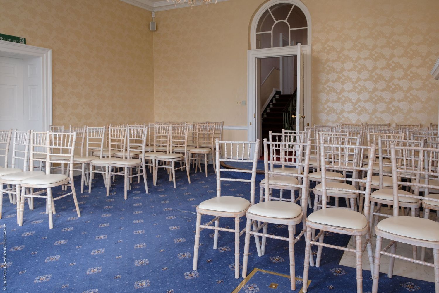 Elegant event room with white Chiavari chairs arranged on blue patterned carpet in a classic cream-walled venue.