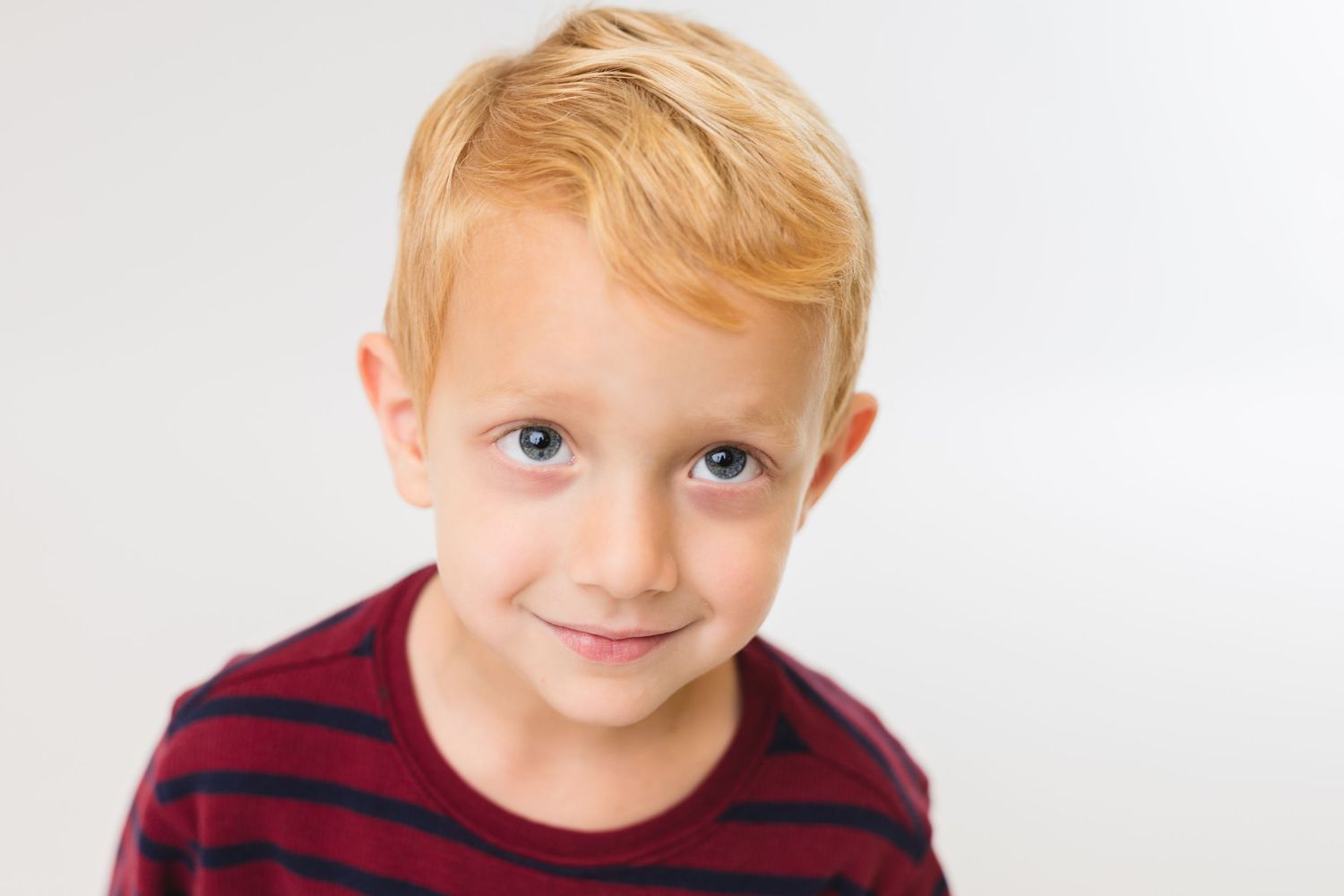 Studio portrait of a child in a burgundy sweater with curly hair and hair clips.