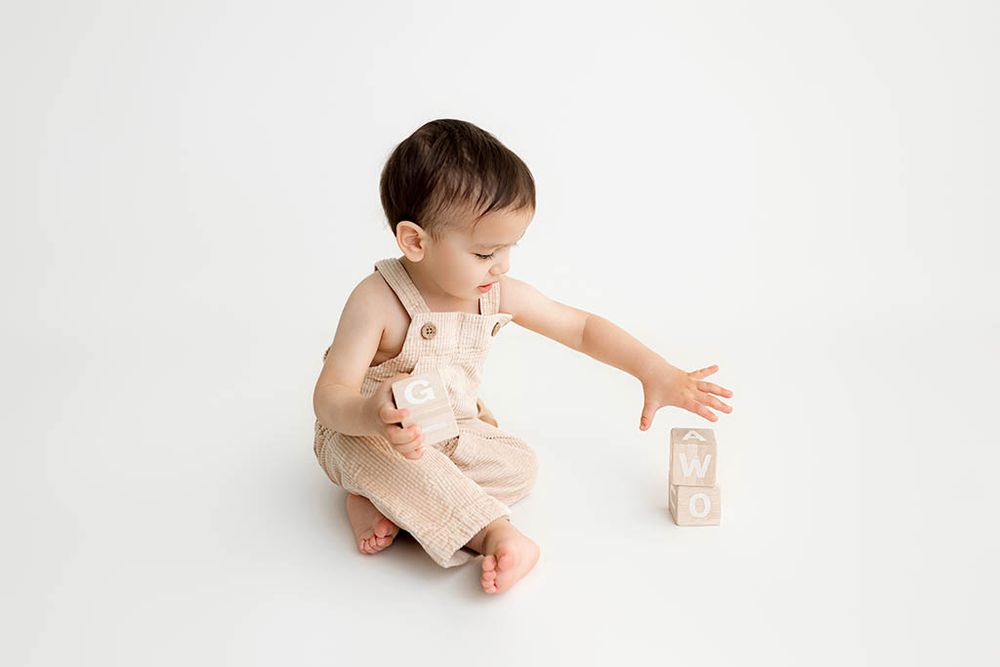 Cute little boy in overalls playing wooden blocks on white background by Menifee children's photographer.