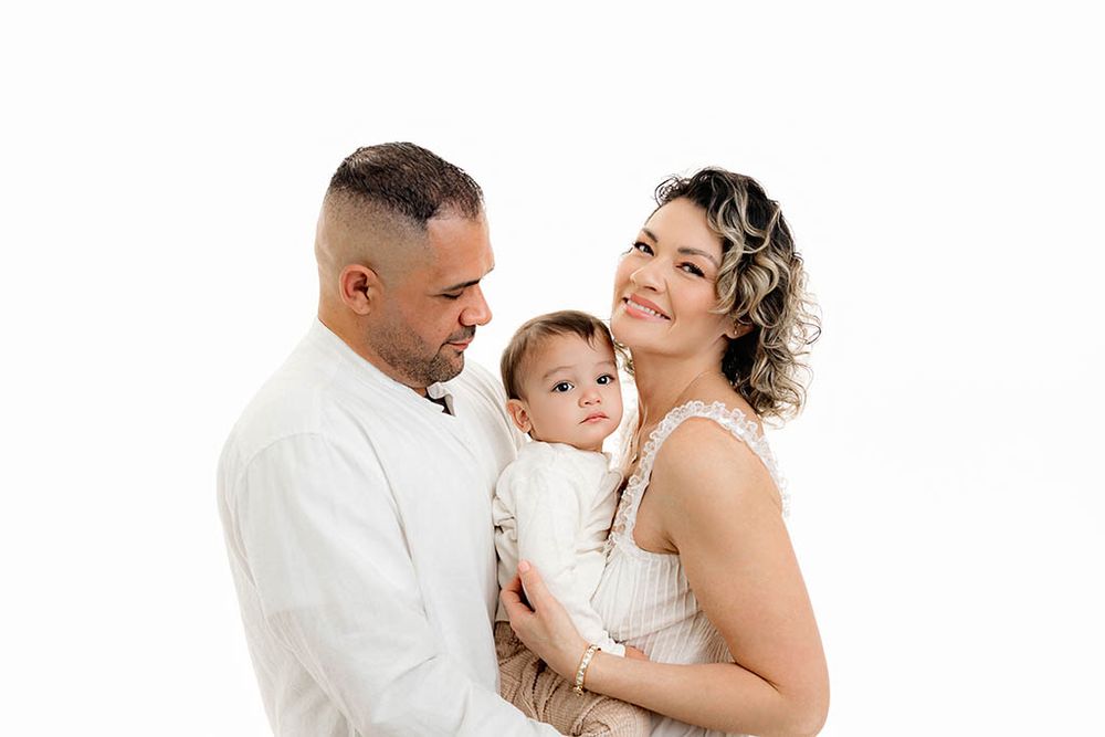 Family portrait of parents holding their little boy for 2nd birthday photos against a clean white background.