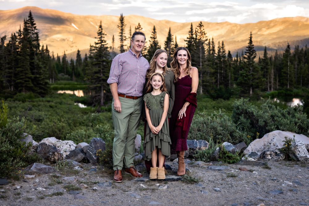 Family of four posing outdoors at golden hour with mountain forest backdrop in Colorado wilderness.