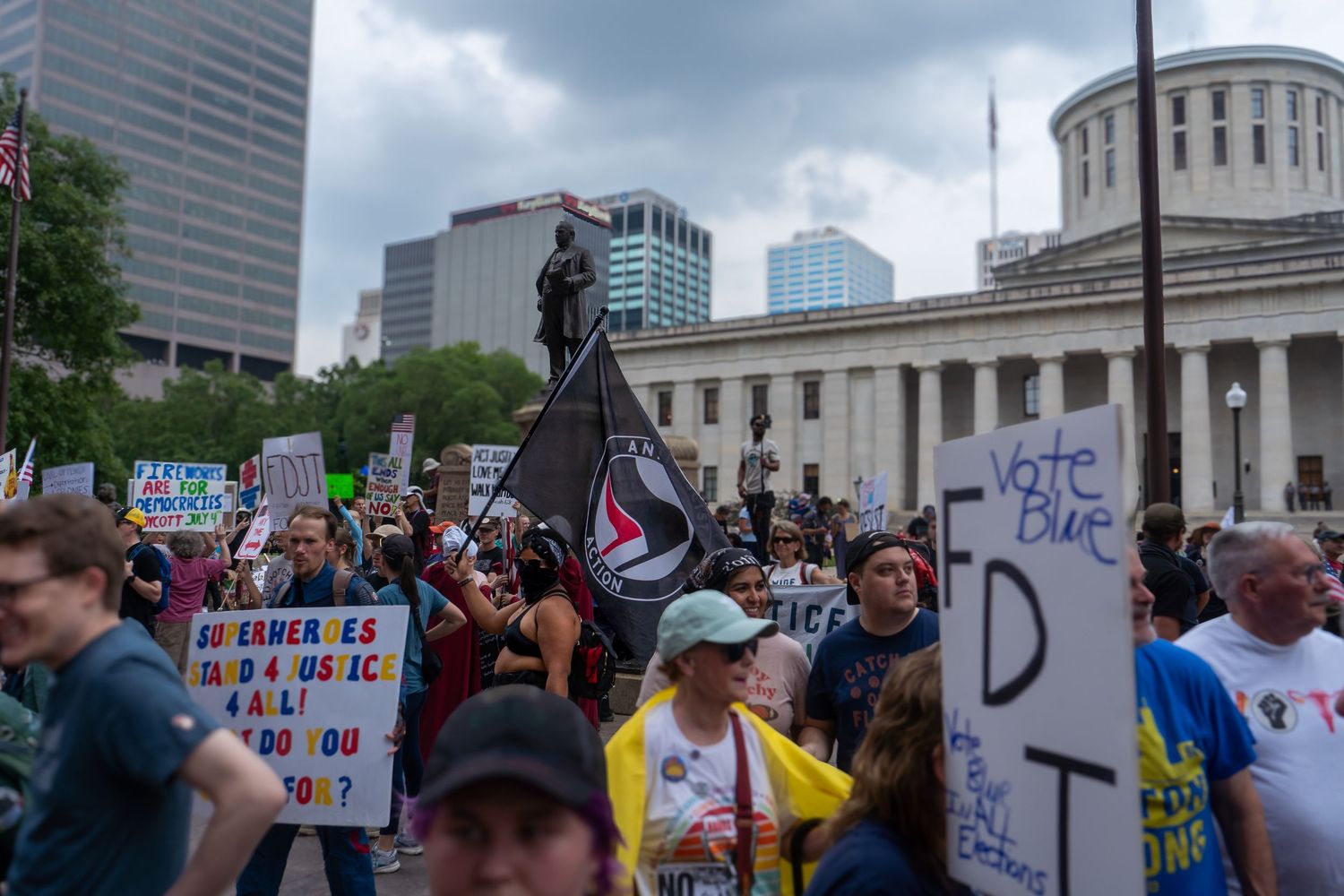Protesters gather outside a government building in an urban area holding signs during a demonstration.