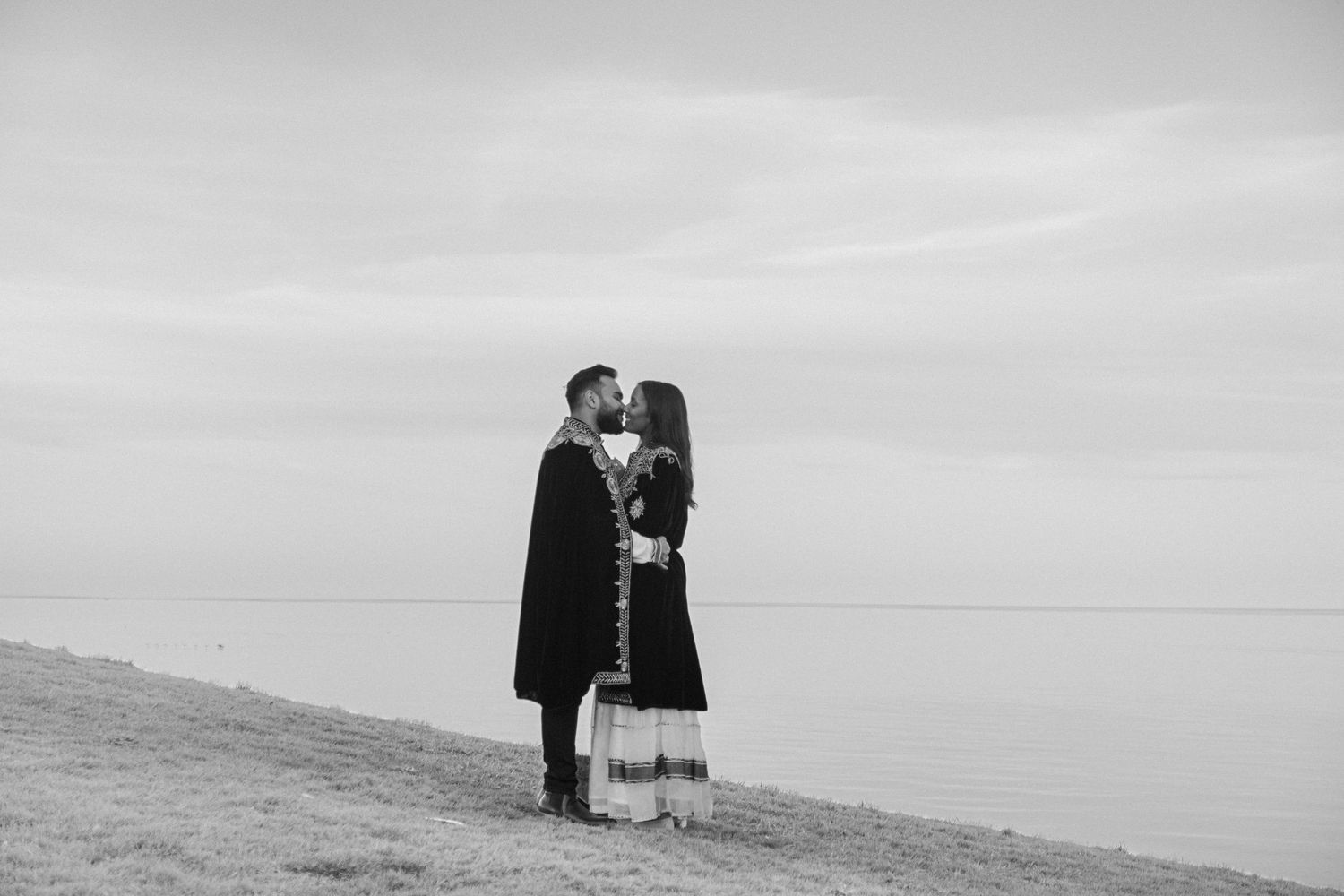 Black and white photo of a bride and groom posing beside a white Rolls-Royce Ghost on their wedding day.