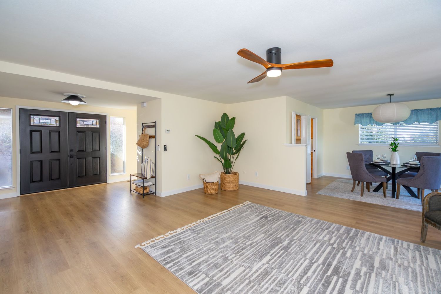 Bright open living room with hardwood floors, ceiling fan, large area rug, and view into dining room with natural light.