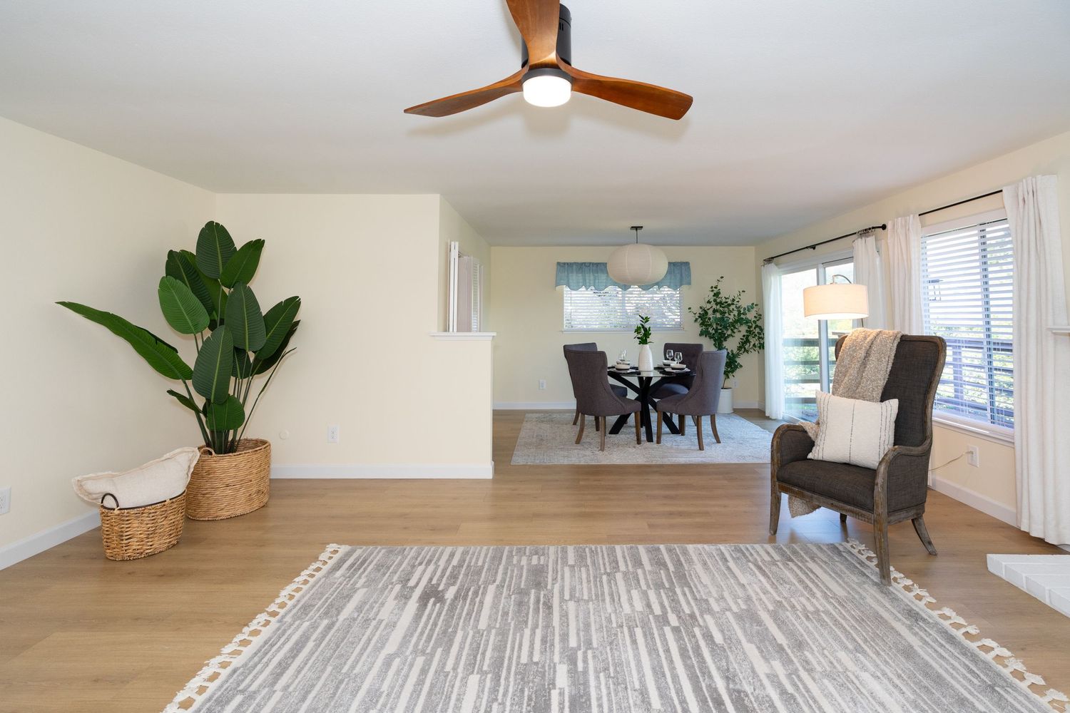 Bright open living and dining room with hardwood floors, ceiling fan, large plant, and sliding glass doors to patio.