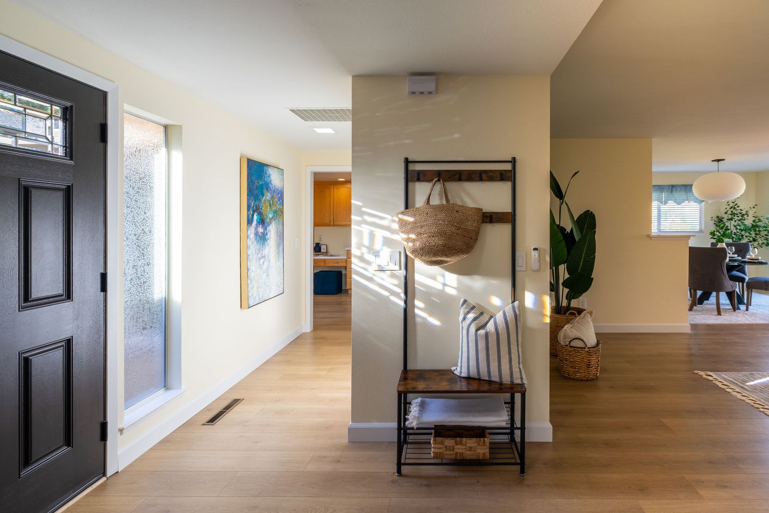 Modern home entryway with hardwood floors, black front door, coat rack, and open floor plan leading to living and dining areas.