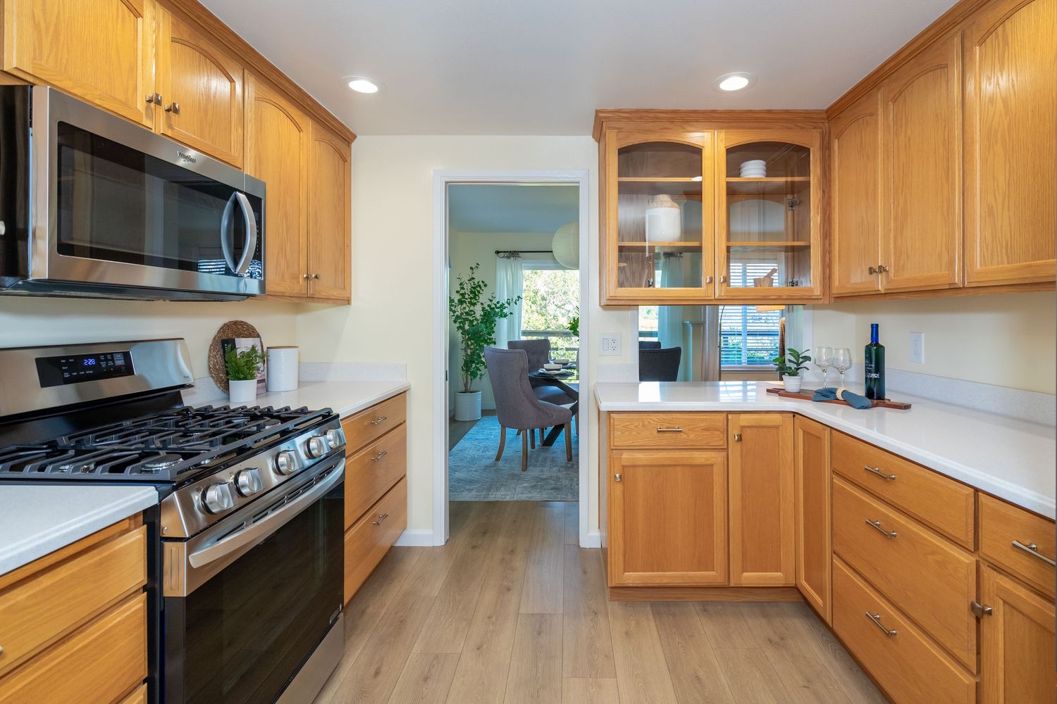 Modern kitchen with honey oak cabinets, stainless steel appliances, gas range, and light hardwood floors opening to dining area.