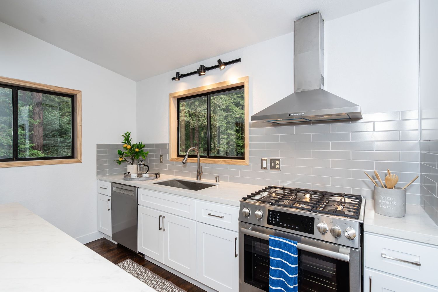 Modern white kitchen with stainless steel range, subway tile backsplash, wall-mounted hood vent, and garden window over sink.