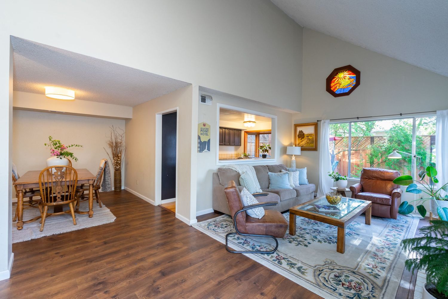Bright open-concept living and dining room with hardwood floors, vaulted ceilings, and large windows allowing natural light.