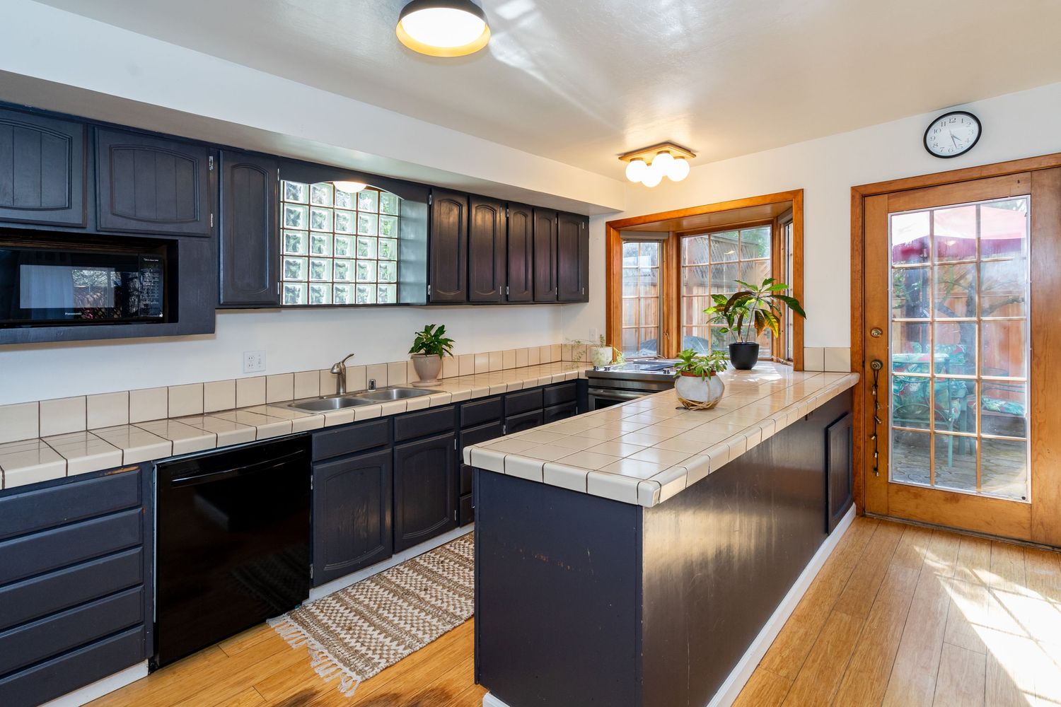 Modern kitchen with dark cabinets, tile countertops, center island, hardwood floors, and natural light from French doors.