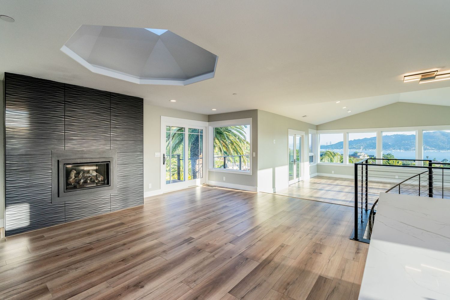 Modern open living room with hardwood floors, tiled fireplace, tray ceiling, and panoramic mountain views through large windows.