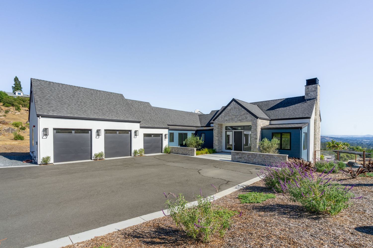Spacious ranch-style home with three-car garage, circular driveway, and panoramic hillside views under clear blue skies.