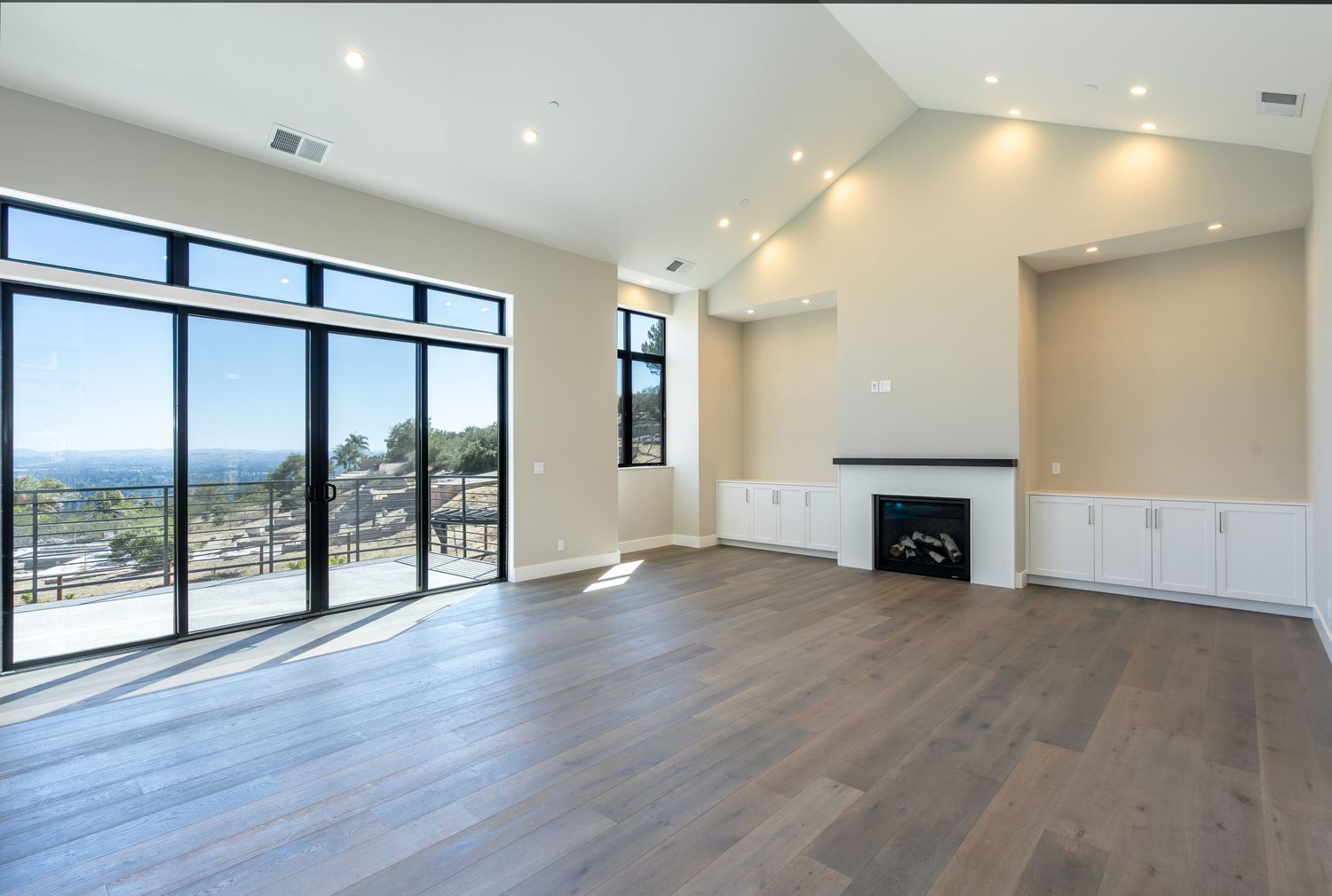 Bright modern living room with hardwood floors, fireplace, built-in cabinets, and large glass doors offering scenic outdoor views.