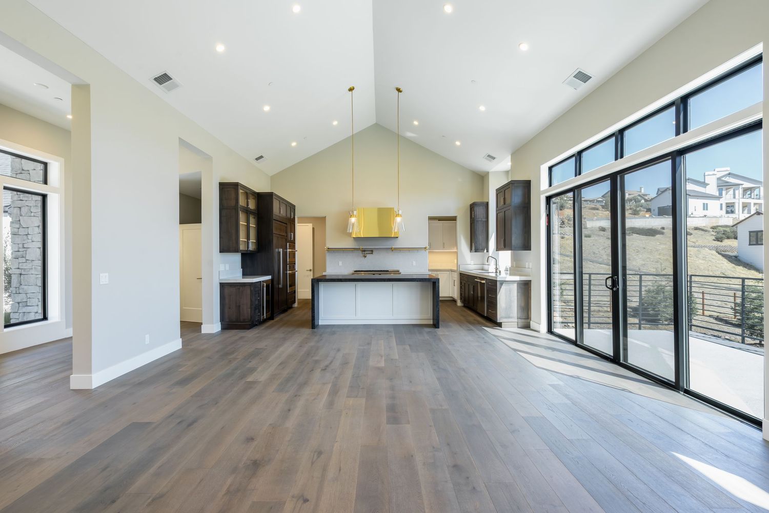 Modern open-concept kitchen with dark cabinets, large island, hardwood floors, and floor-to-ceiling windows in a new home.