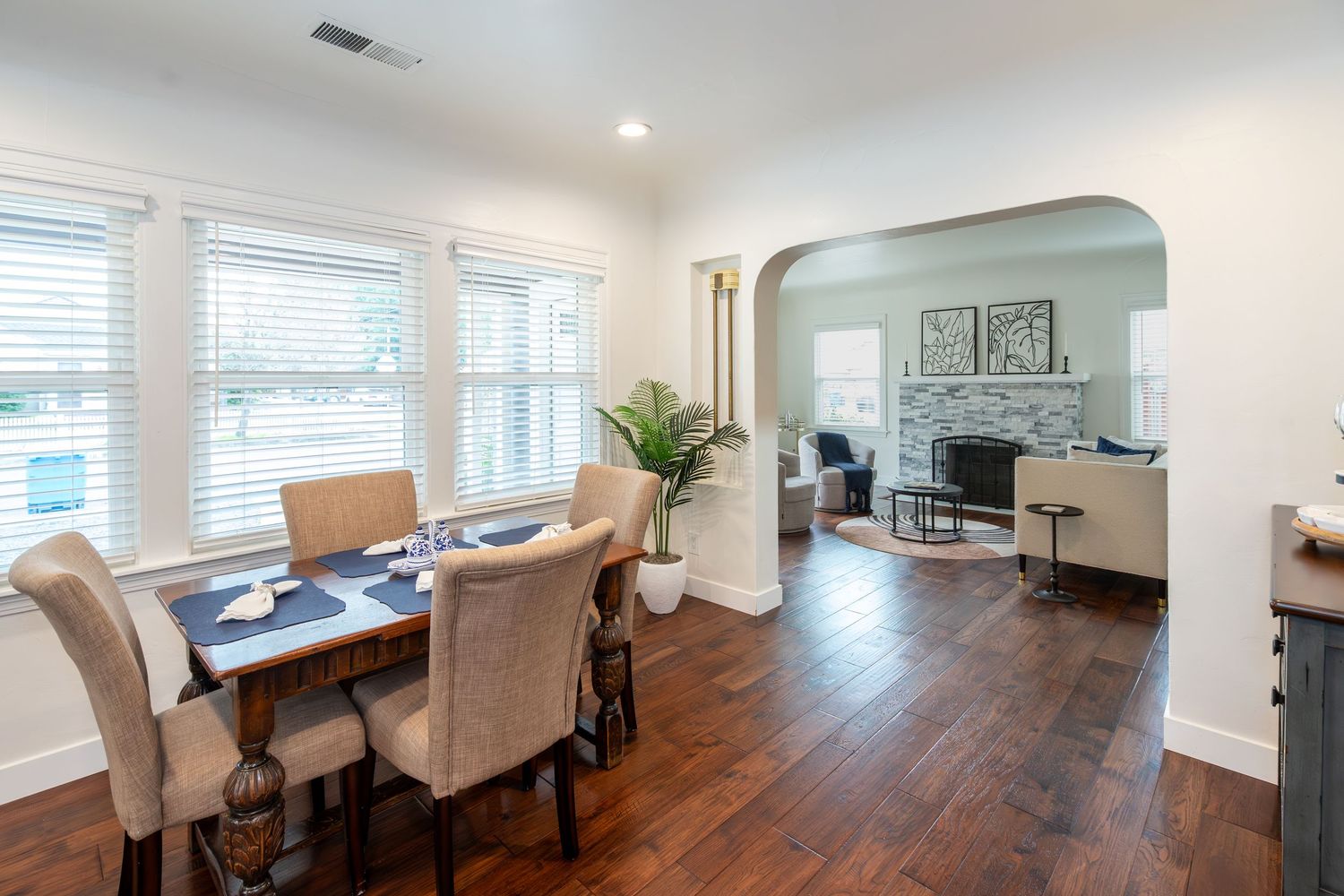 Bright dining room with hardwood floors, white trim, and an arched doorway leading to a cozy living room with a fireplace.