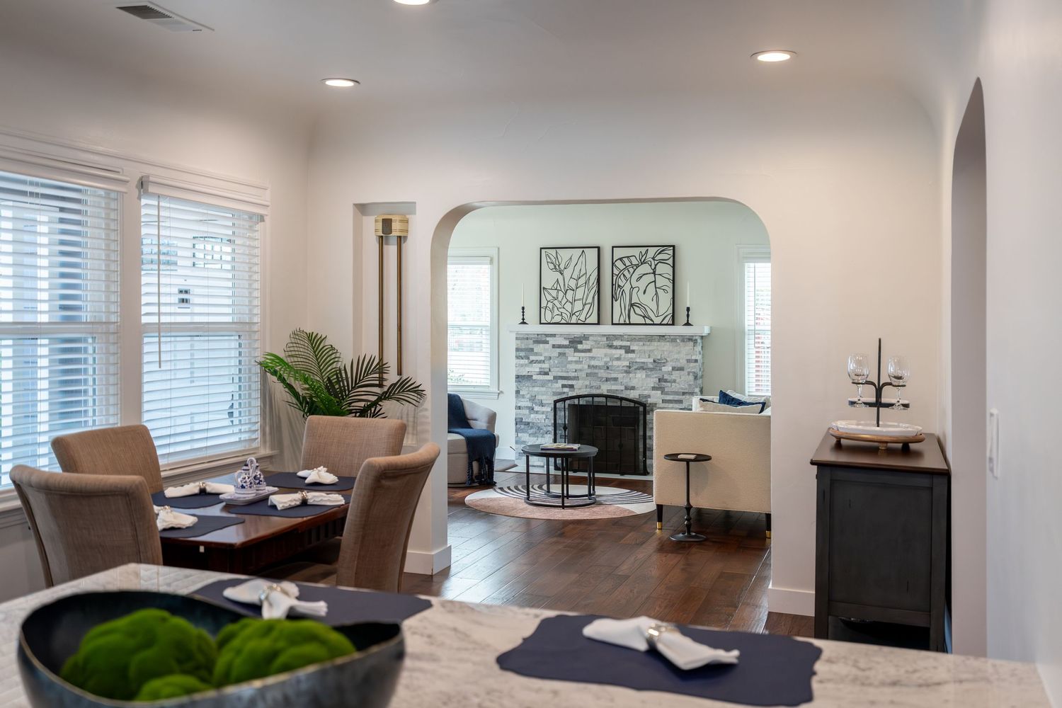 Open-concept living room with stone fireplace, arched doorway, hardwood floors, and neutral decor in a modern home.