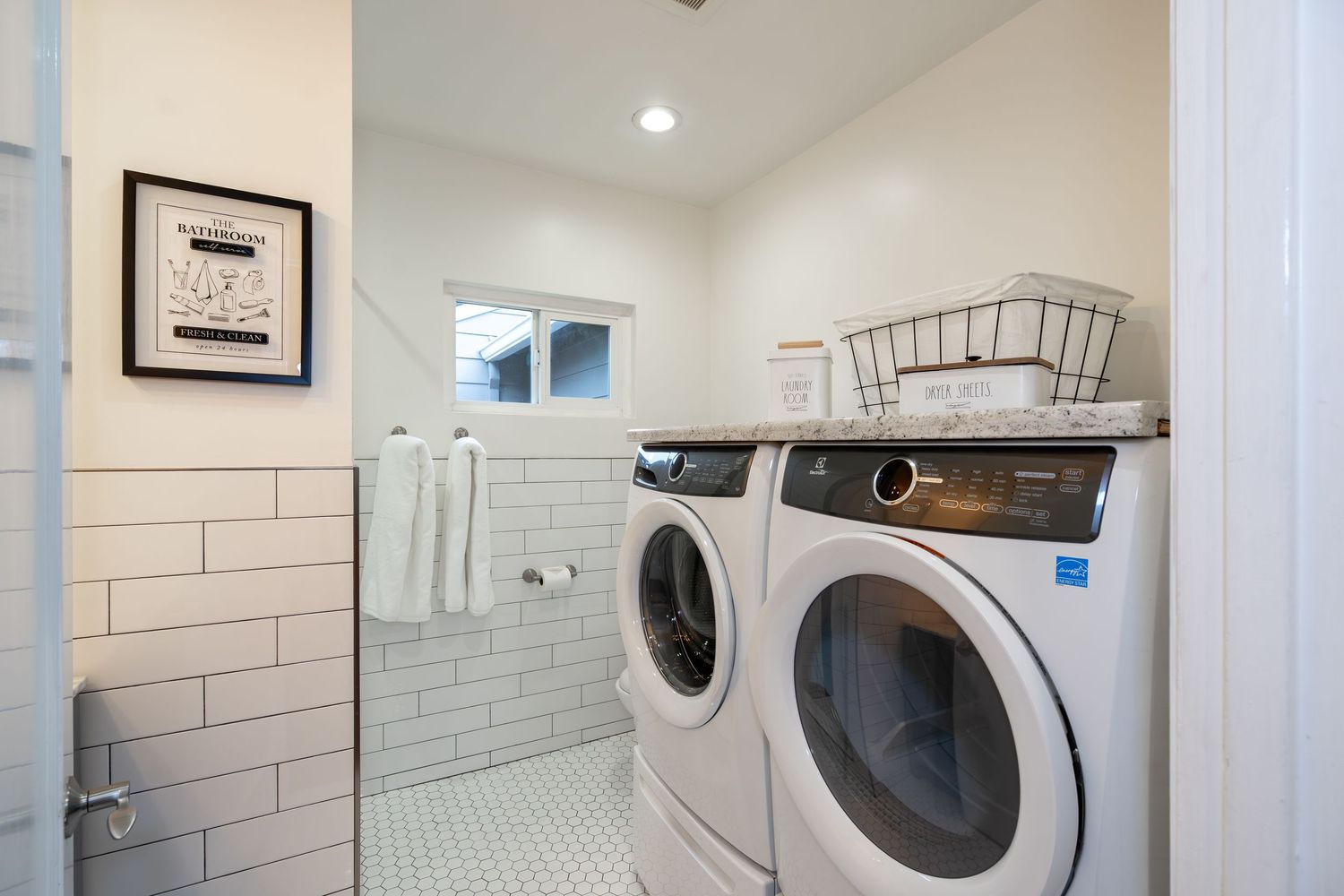 Modern laundry room with white front-load washer and dryer, subway tile walls, and basket storage on top.