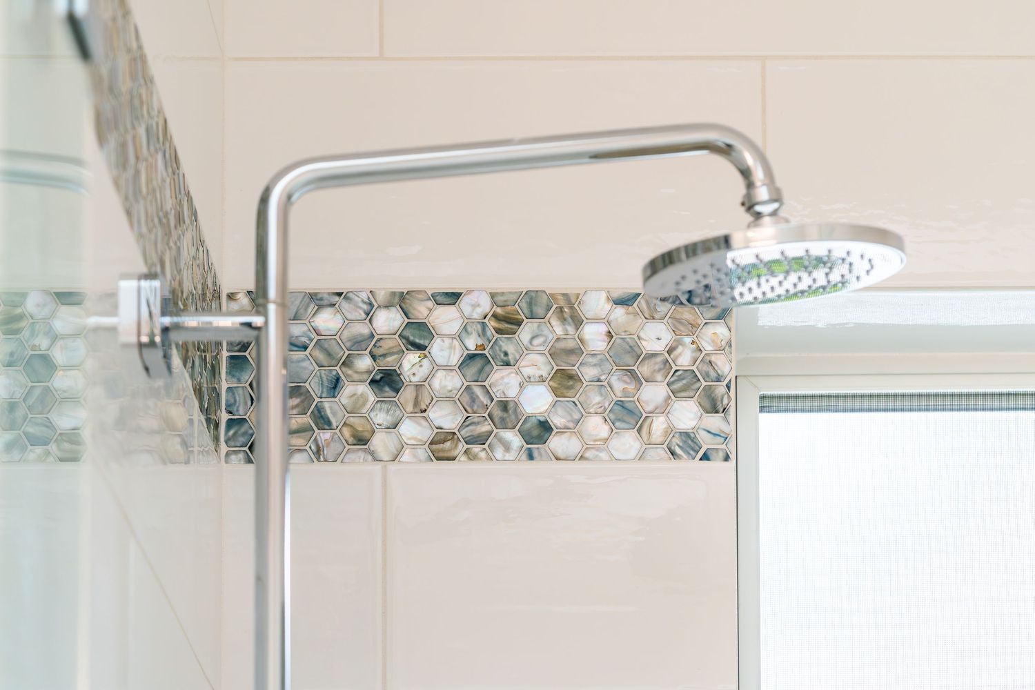 Modern chrome rain shower head mounted on tiled wall with decorative hexagon mosaic tile border in bathroom.