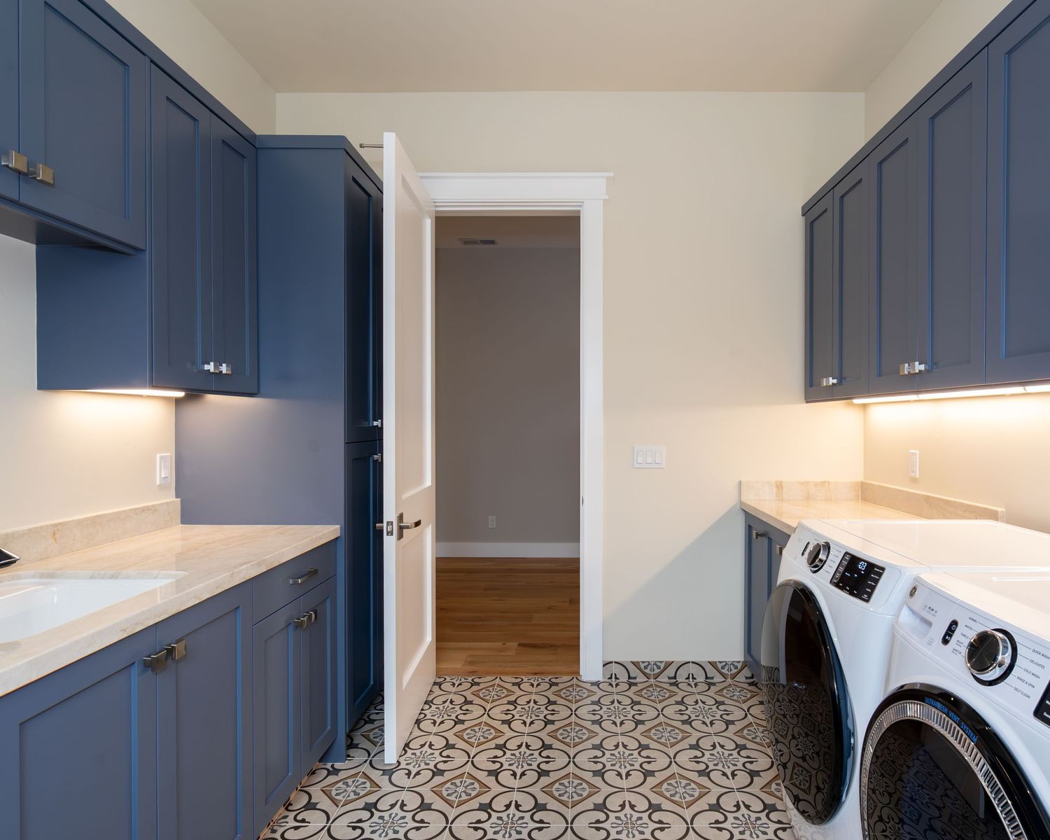 Laundry room with navy blue cabinets, white washer and dryer, marble countertops, and decorative patterned tile flooring.