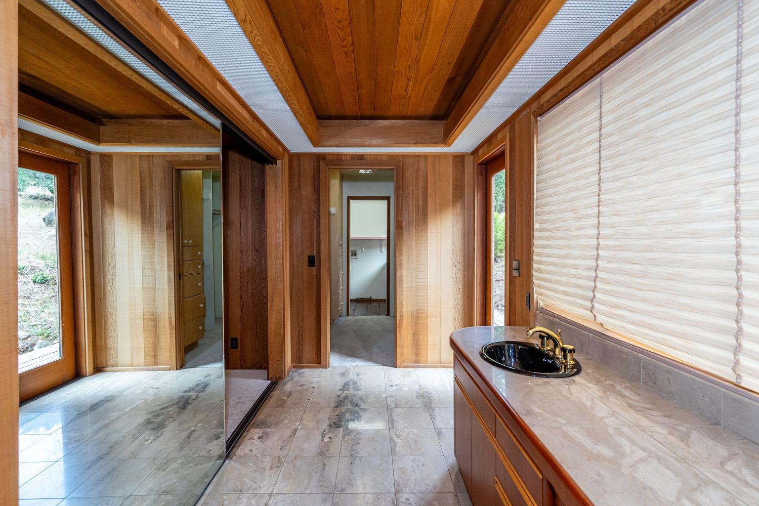 Wood-paneled hallway with marble floors, mirrored sliding doors, built-in sink vanity, and natural light from large windows.