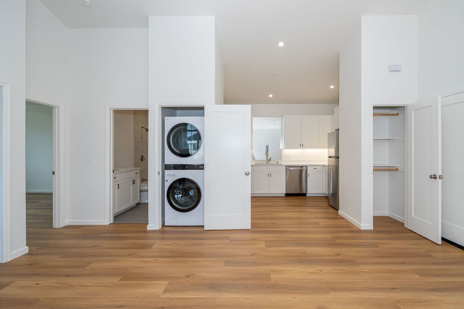 Modern open-plan apartment with stacked washer-dryer, hardwood floors, white cabinets, and open kitchen in background.