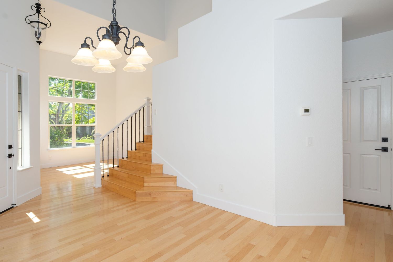 Bright foyer with hardwood floors, elegant chandelier, white walls, and staircase with wood steps leading to upper level.