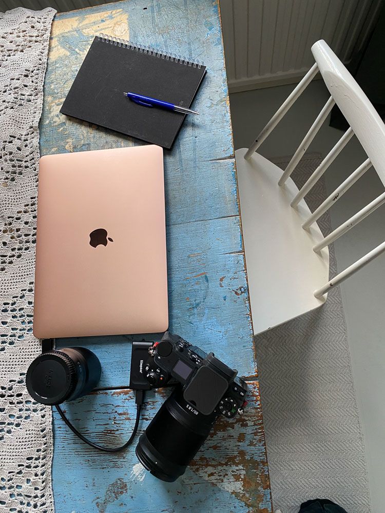 En av arbetsplatserna för Fotograf Jessica Lindqvist - köksbordet i hemmet. Dator, block, kamera och objektiv sett uppifrån.