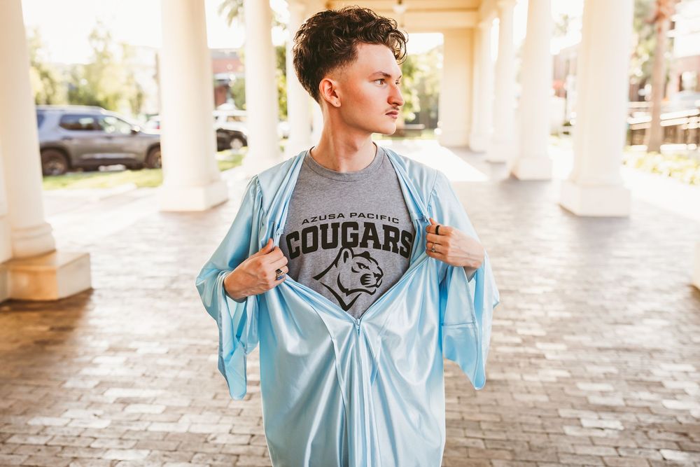 Young man revealing an Azusa Pacific Cougars t-shirt under a light blue jacket for senior photos in redlands