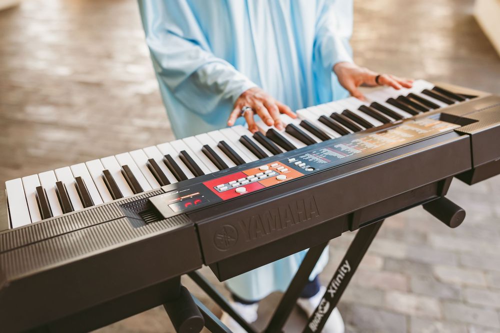 Person in blue outfit playing a Yamaha electronic keyboard on a stand indoors.