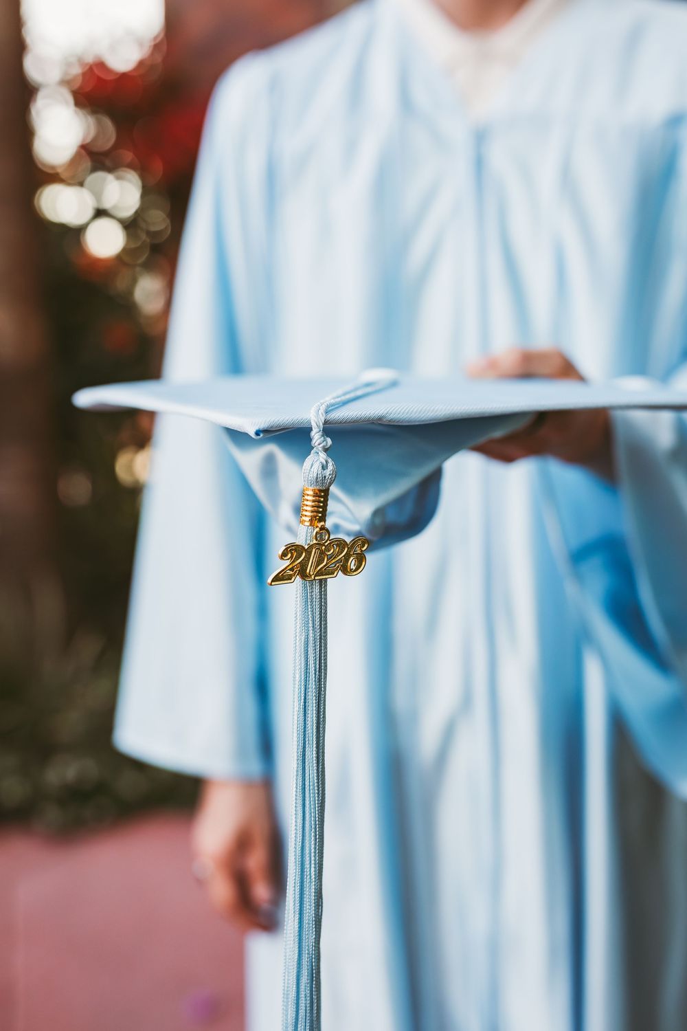 Close-up of a light blue 2026 graduation cap with gold tassel held by a graduate in matching gown in downtown redlands senior session