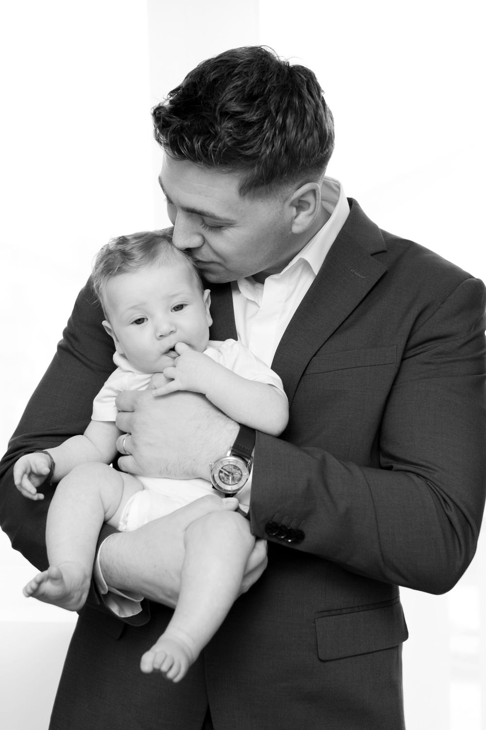 Black and white photo of a man in a suit tenderly kissing a baby he holds in his arms.